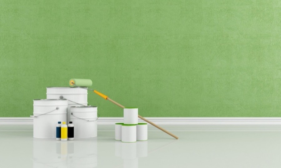 Paint tins, roller and brush in front of a freshly painted green wall